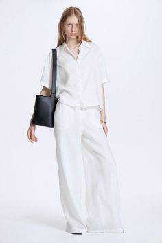 Woman in a white linen shirt and pants with a black shoulder bag