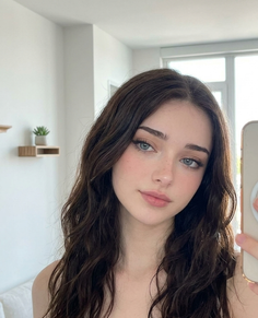 Young woman with long dark hair and blue eyes taking a selfie indoors
