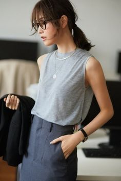 Woman with a ponytail and glasses wearing a sleeveless top and trousers indoors