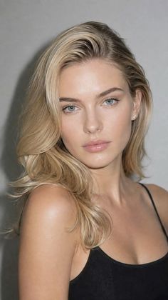 Woman with blonde hair and blue eyes wearing a black top, looking directly at the viewer