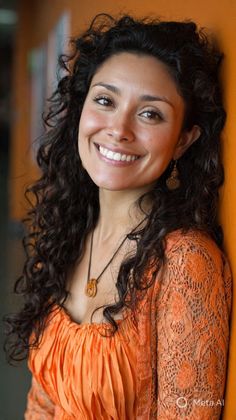 Woman with curly hair and an orange top smiling against an orange wall