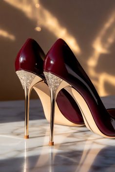 Pair of burgundy patent leather high heels with gold and rhinestone heels on a marble surface