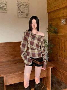 Woman with long black hair wearing a plaid shirt and black shorts indoors