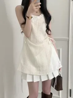 Woman in a white lace top and pleated skirt holding a handbag indoors