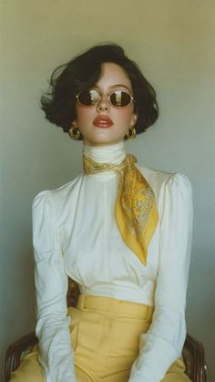 Woman with short hair and sunglasses wearing a white blouse and yellow scarf