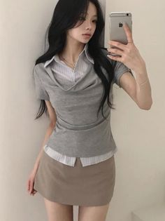 Woman with long black hair taking a mirror selfie in a grey top and mini skirt