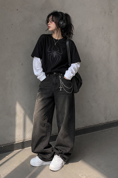 Person in a black t-shirt with a spider graphic, baggy jeans, and headphones
