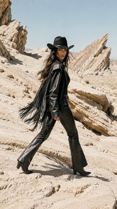Woman in a black cowboy hat and leather outfit walking in a desert landscape