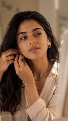 Woman with long dark hair putting on gold hoop earrings