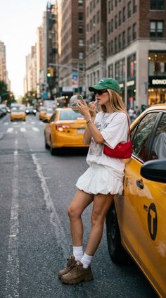 Woman in a white dress and green cap applying lipstick on a city street