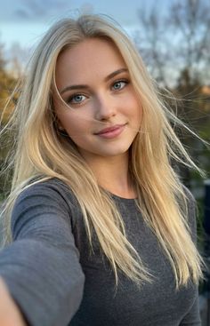 Blonde woman with blue eyes and long hair in a grey shirt outdoors