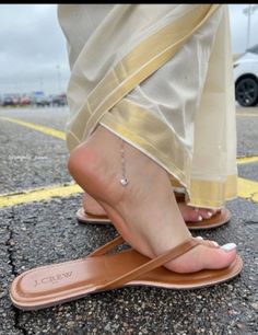Close up of bare feet in flip flops with an anklet on wet ground