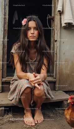 Young woman with long brown hair and a pink flower in her hair, sitting barefoot