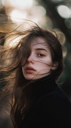 Woman with long, windblown hair wearing a black turtleneck, with backlight