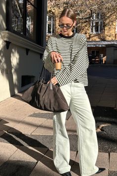 Woman in a striped shirt and wide leg jeans holding a coffee cup on a sunny street