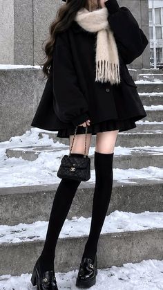 Person in a black coat and mini skirt with knee-high socks on snowy stairs