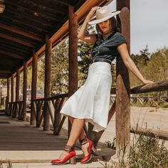 Woman in a cowboy hat, white skirt, and red shoes on a wooden porch