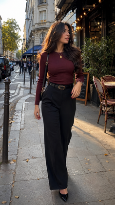 Woman with long hair in a burgundy top and black pants walking on a street
