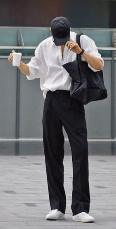 Person in a white shirt, black pants, and baseball cap holding a coffee cup