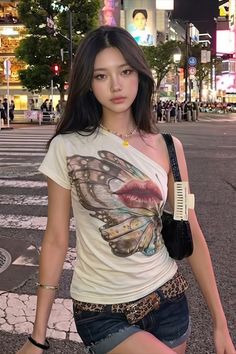 Woman with long hair wearing a one-shoulder top and denim shorts on a city street at night