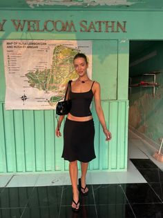 Woman in a black top and skirt standing in front of a map