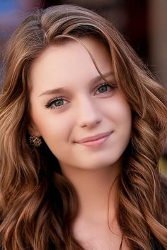 Young woman with long wavy brown hair and green eyes, smiling at the camera