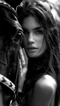 Woman with long hair leaning against a horse in a black and white portrait
