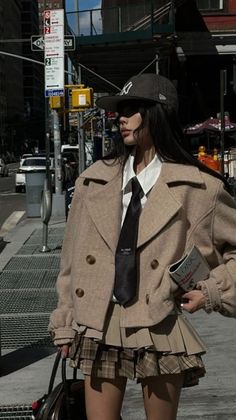 Woman in a peacoat, pleated skirt, and baseball cap on a city street