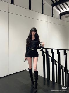 Woman with long black hair wearing a black shirt and shorts with knee-high boots