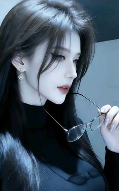 Woman with long black hair holding glasses, wearing a black turtleneck