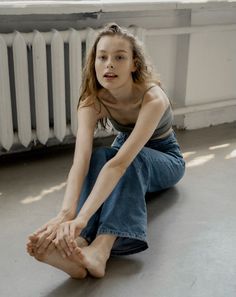 Young woman with long hair sitting on the floor in jeans and a spaghetti strap top