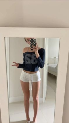 Person in white shorts and a long sleeve shirt taking a mirror selfie