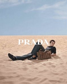 Man in jeans and a black shirt lying on sand with a brown bag