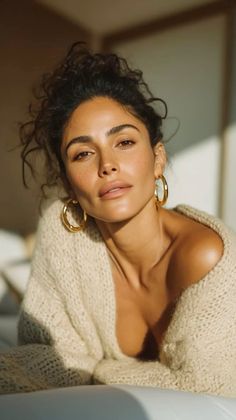 Woman with curly hair and freckles wearing a beige sweater and gold hoop earrings