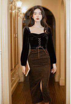 Woman in a black velvet top and brown corduroy skirt holding a book indoors