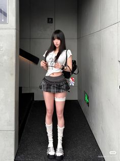 Woman with long black hair wearing a plaid skirt and crop top indoors