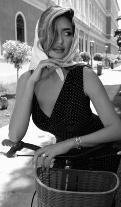 Woman in a polka dot dress and headscarf leaning on a bicycle