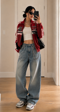 Woman in a red racing jacket, crop top, and baggy jeans taking a mirror selfie