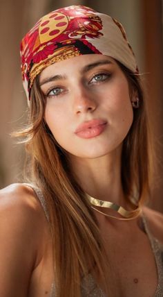 Woman with a patterned head scarf and gold choker looking at the camera