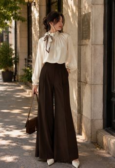 Woman in a white blouse and brown wide-leg pants standing outdoors
