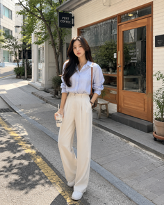 Woman in a striped shirt and wide leg pants standing on a street in front of a coffee shop