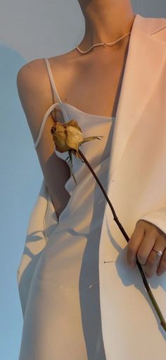 Person in a white blazer and slip dress holding a dried rose