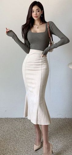 Woman with long dark hair wearing a long sleeve top and midi skirt indoors