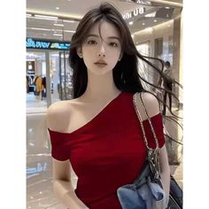 Woman with long dark hair wearing a red off-shoulder top and carrying a shoulder bag