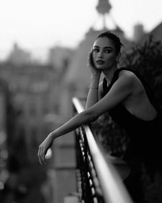 Woman in a black top leaning on a balcony railing overlooking a cityscape