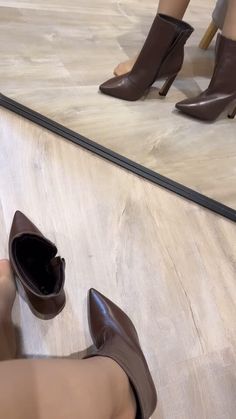 Person trying on brown high-heeled boots on a wooden floor with a mirror reflection