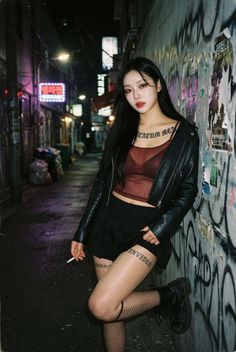Woman in a leather jacket and mini skirt leaning against a graffiti wall at night