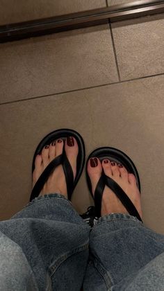 Person wearing black flip flops and blue jeans on a tiled floor