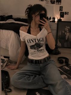Woman in an off-shoulder top and baggy jeans taking a mirror selfie in a bedroom