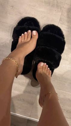 Feet with white french pedicure, gold anklet, and toe ring wearing black fuzzy slippers